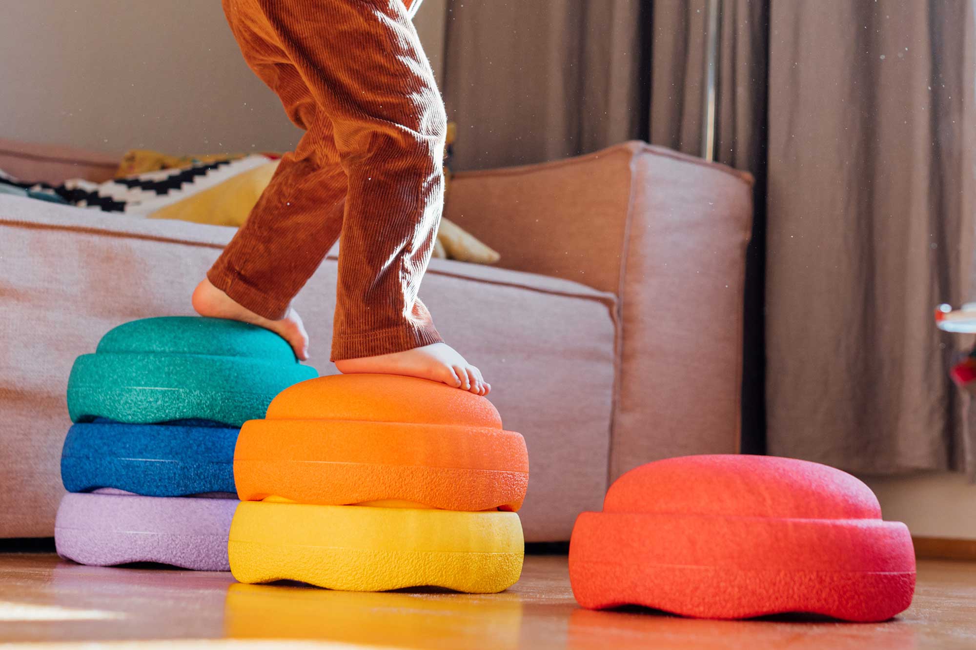 Kind steigt auf bunt gestapelte Stapelsteine in Regenbogenfarben
